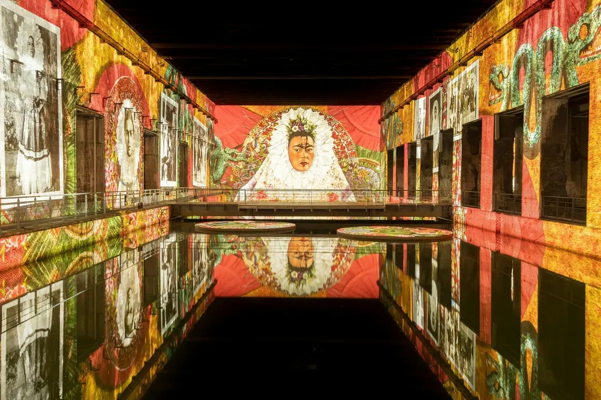 Un intérieur décoratif orné de fresques colorées représentant des visages et des motifs, qui se reflètent symétriquement dans un plan d'eau calme.