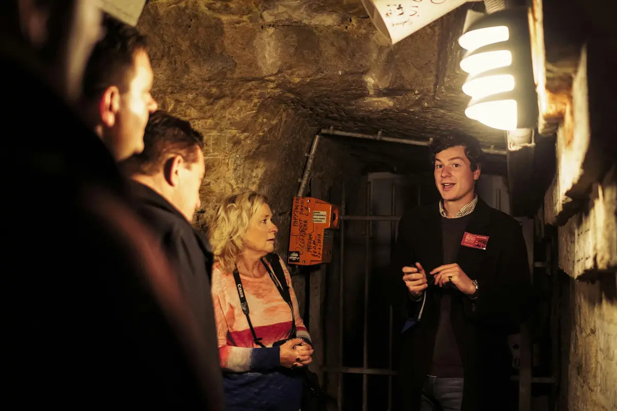 Un groupe de personnes dans un lieu souterrain faiblement éclairé, avec un guide qui donne des explications au groupe.