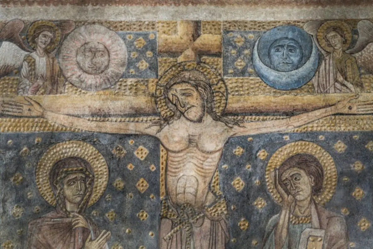 Fresque médiévale représentant la crucifixion de Jésus avec deux pleureuses et les visages symboliques du soleil et de la lune au-dessus.