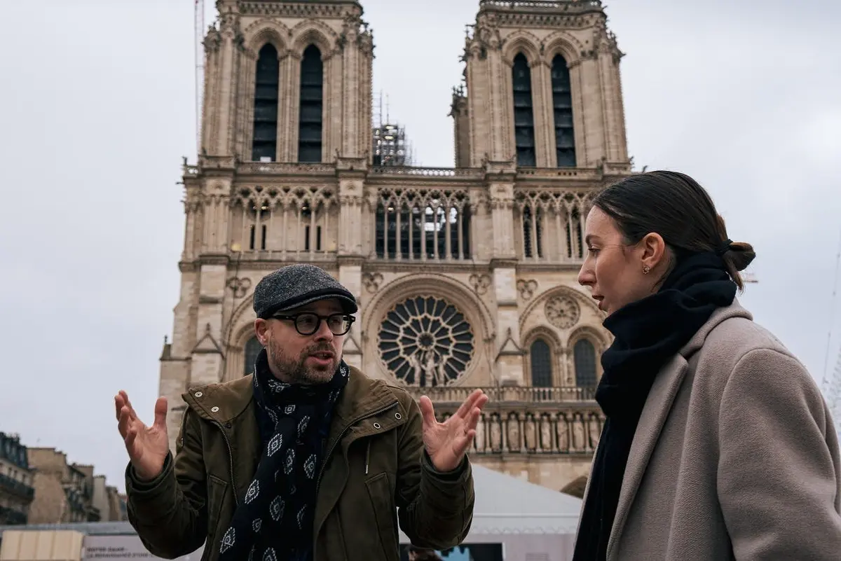 Deux personnes discutent devant une cathédrale gothique à l'architecture ornée et à la grande rosace.
