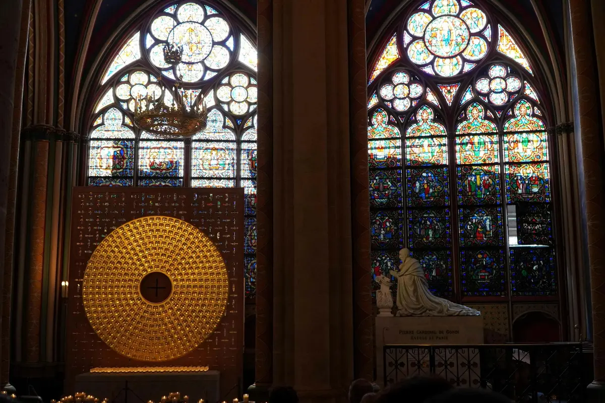 Des vitraux aux motifs complexes côtoient un autel circulaire doré et une statue à l'intérieur d'une cathédrale faiblement éclairée.