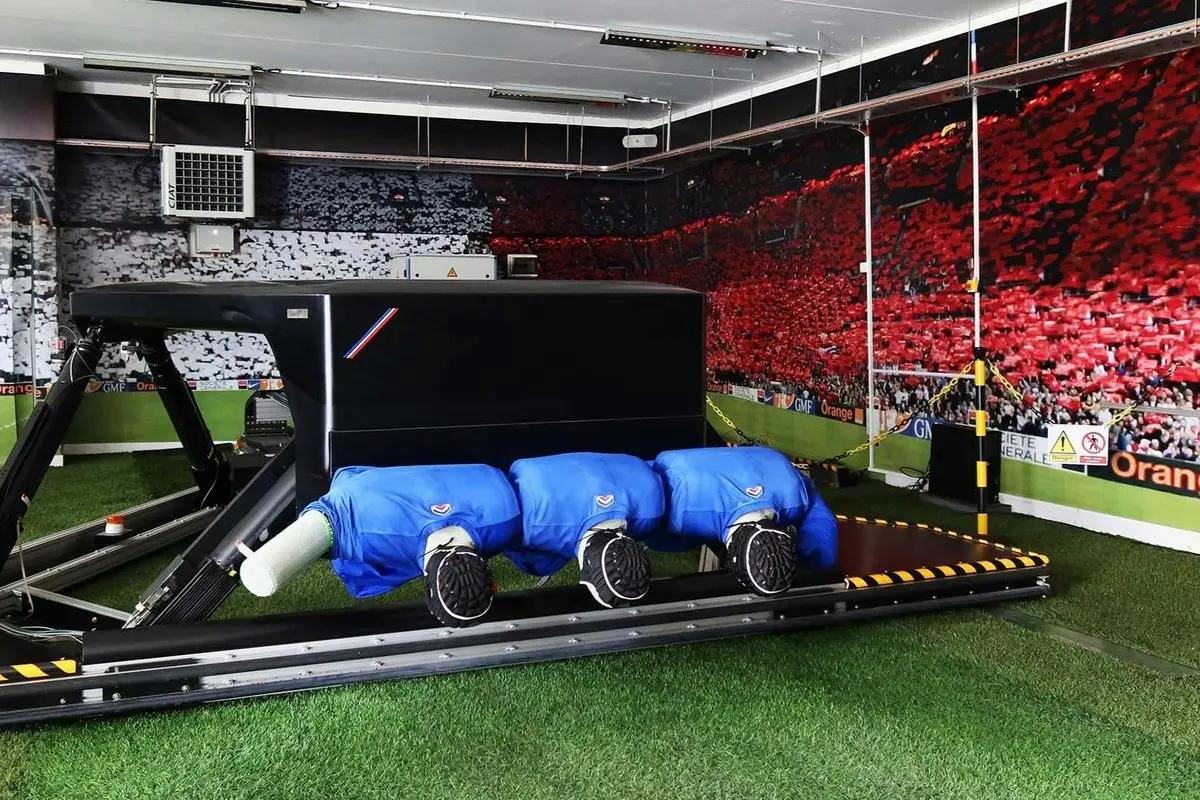 Un simulateur d'entraînement équipé de sièges rembourrés et de gazon artificiel, installé à l'intérieur devant un mur décoré sur le thème d'un stade.