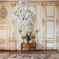 Pièce ornée de détails dorés, d'un grand lustre en cristal, d'un mur en miroir et d'une table en bois avec un buste et des chandeliers. &copy; Sophie Lloyd