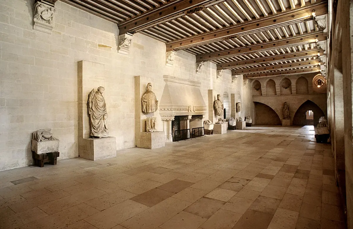 Hall d'entrée spacieux avec statues en pierre, plafond à poutres apparentes, grande cheminée et alcôve voûtée à l'arrière-plan.