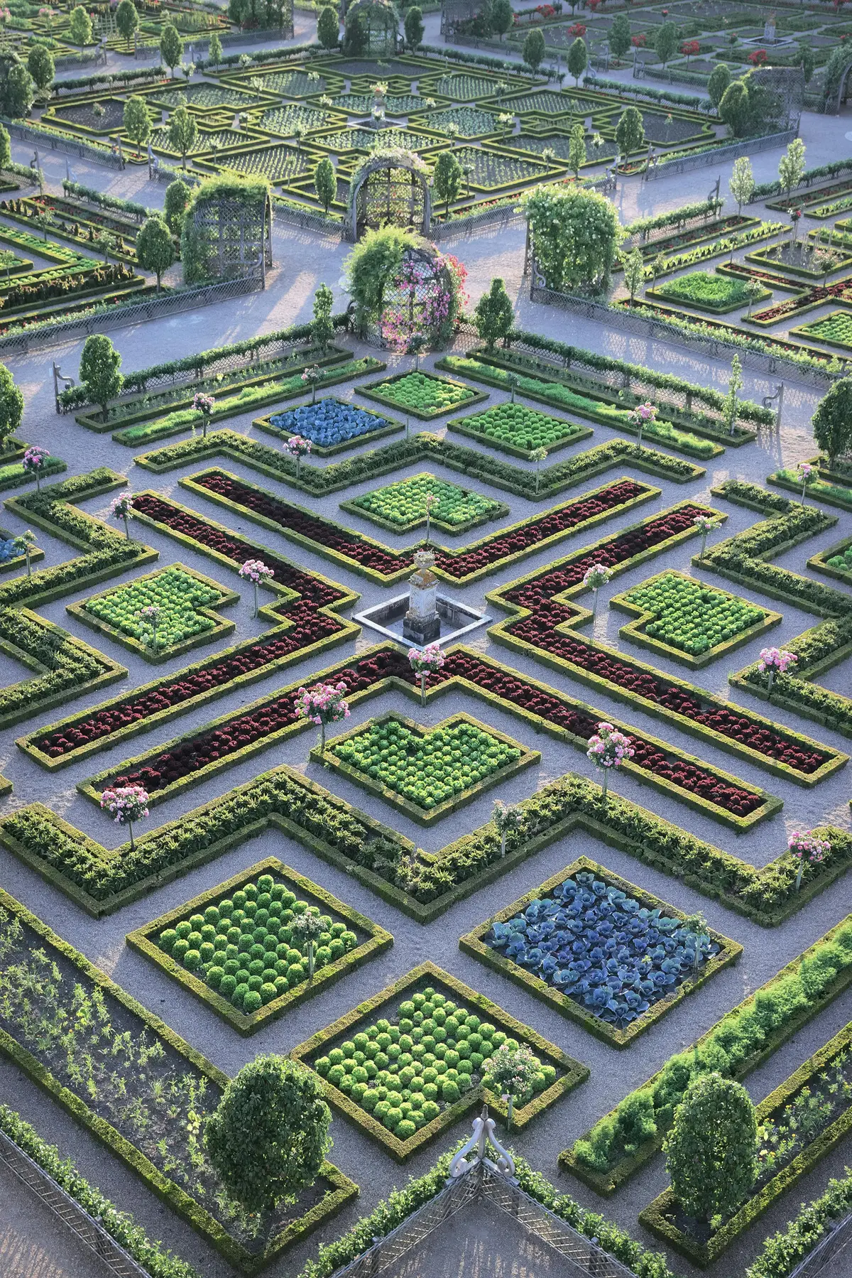 Jardin symétrique avec des parterres de fleurs bien ordonnés et des haies taillées, doté d'une fontaine centrale et d'allées formant un X.