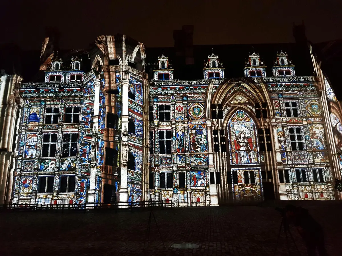 Projection de dessins colorés et complexes sur la façade d'un grand bâtiment de style gothique, la nuit.