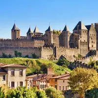 Un château historique aux multiples tours surplombe un village aux maisons colorées et au feuillage vert sous un ciel bleu limpide. © Rolf E. Staerk