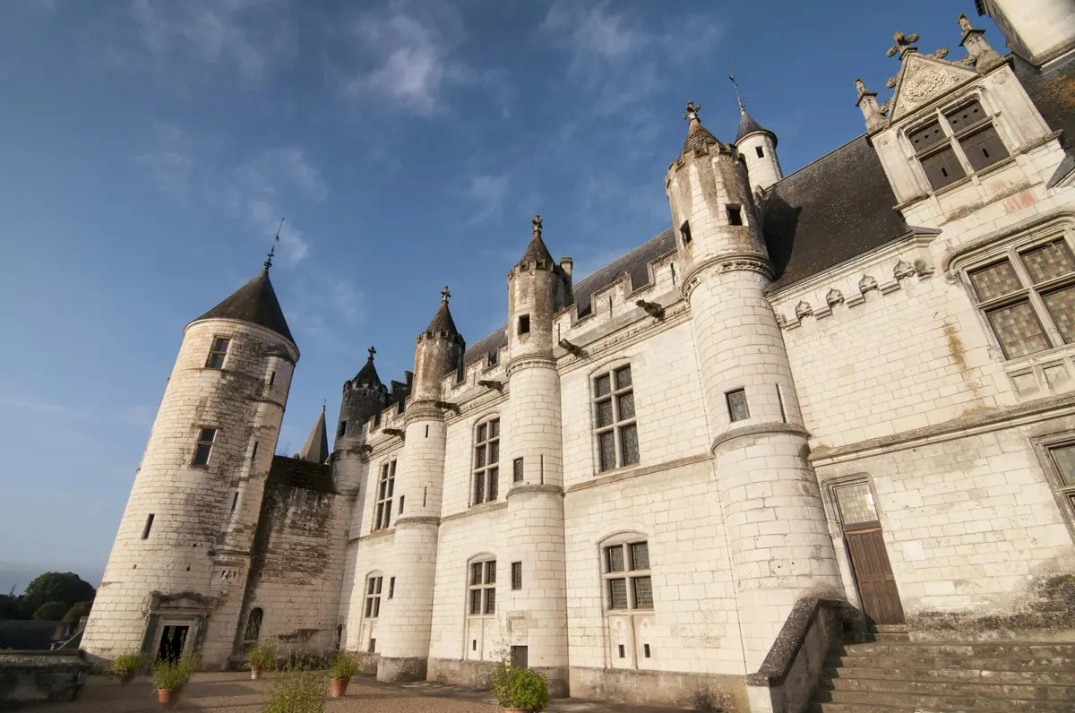 Un château historique en pierre blanche avec de multiples tours et tourelles sous un ciel bleu.