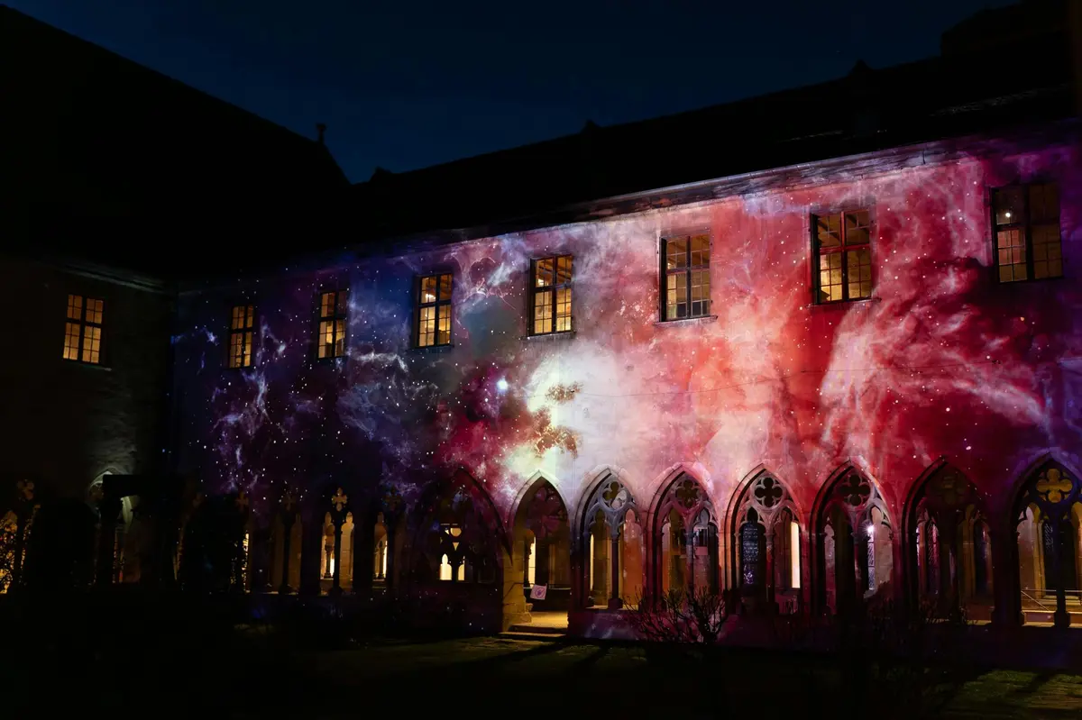 Un bâtiment aux fenêtres cintrées, illuminé la nuit par une projection cosmique aux couleurs éclatantes.