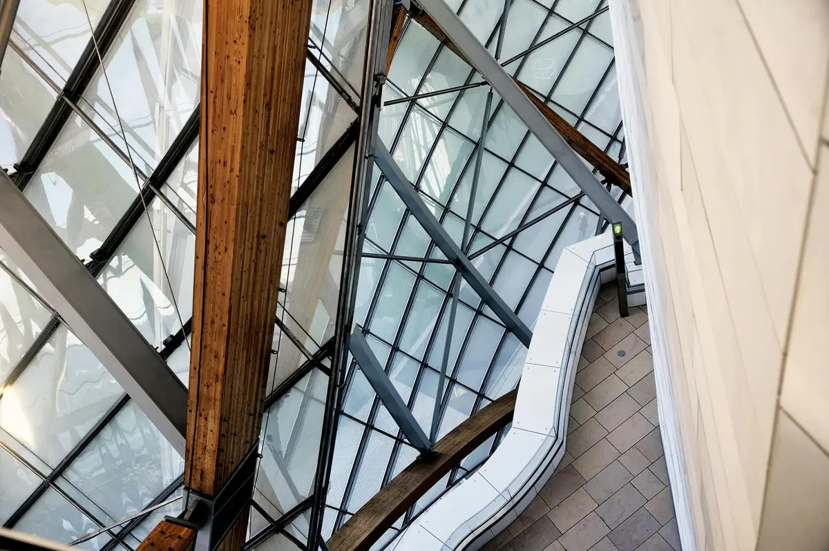 Vue d'une structure architecturale moderne composée de grands panneaux de verre, de poutres en bois et d'une passerelle blanche.