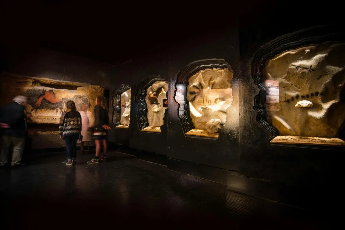 Une exposition faiblement éclairée avec des formations rocheuses et des silhouettes de deux personnes regardant des expositions dans un cadre semblable à celui d'un musée.