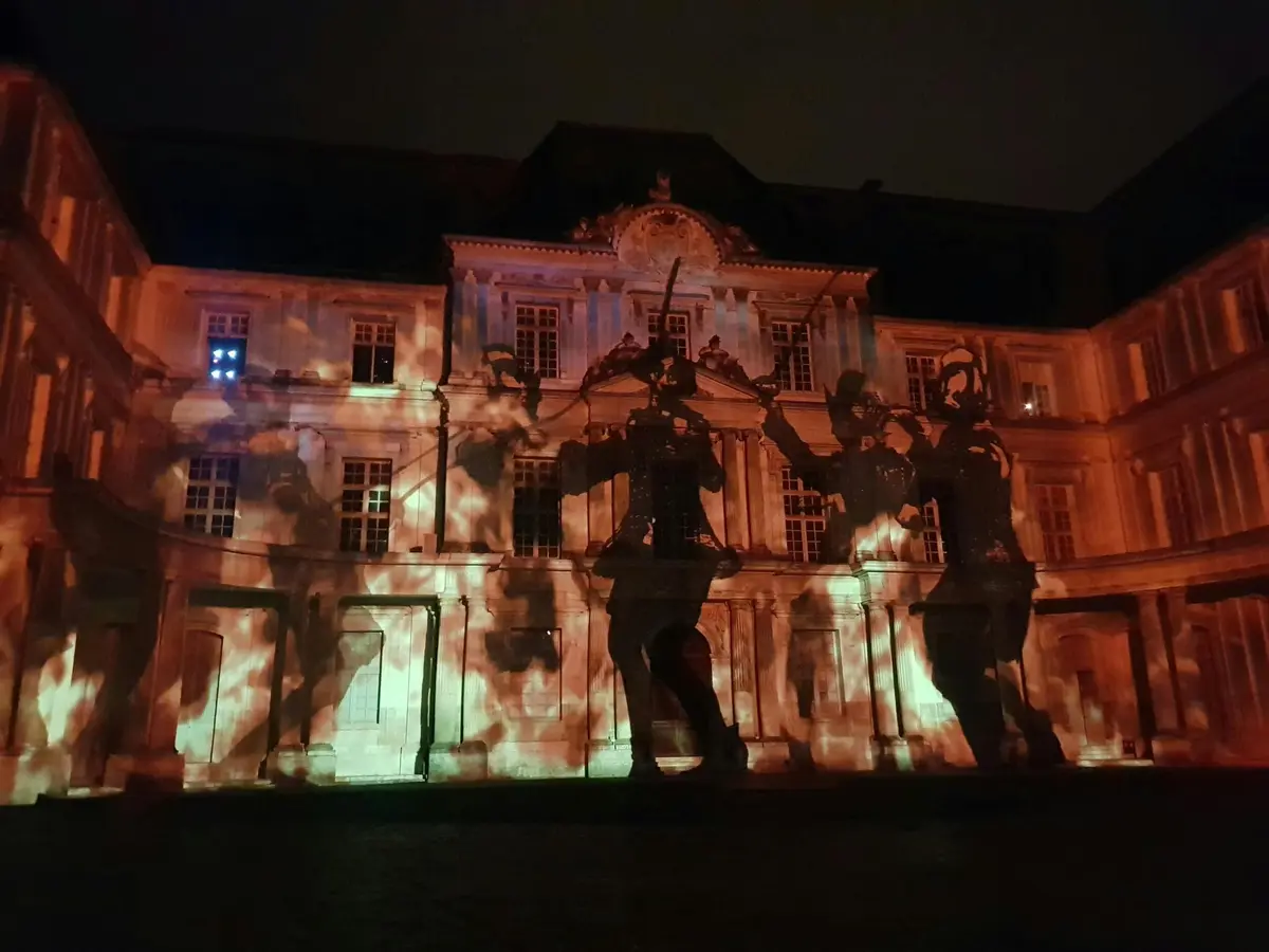 Façade d'un bâtiment historique illuminée la nuit par des images projetées de soldats en marche.