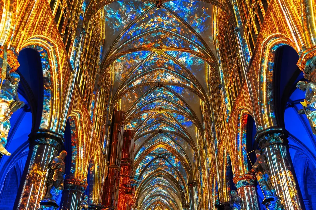 L'intérieur d'une cathédrale, avec ses arches dorées richement décorées et son plafond illuminé de motifs colorés bleus et dorés.