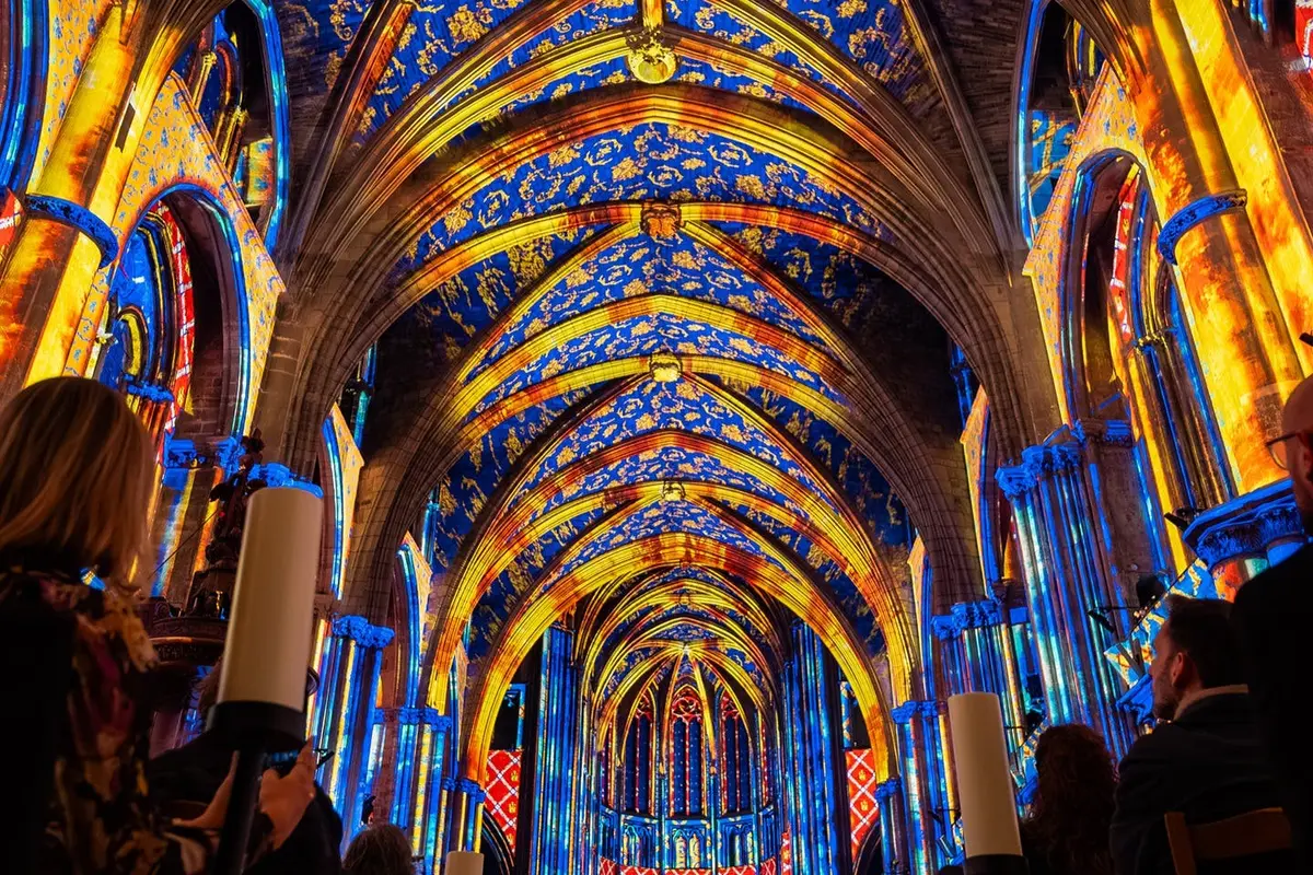 L'intérieur d'une cathédrale éclairé par des projections artistiques colorées, mettant en valeur des motifs complexes sur les arcs et le plafond.