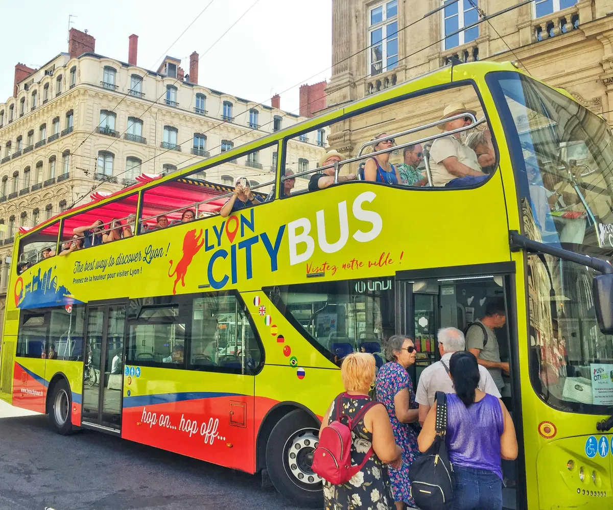 Un autobus touristique à impériale jaune vif et rouge portant l'inscription Lyon City Bus avec des passagers, garé dans un cadre urbain.