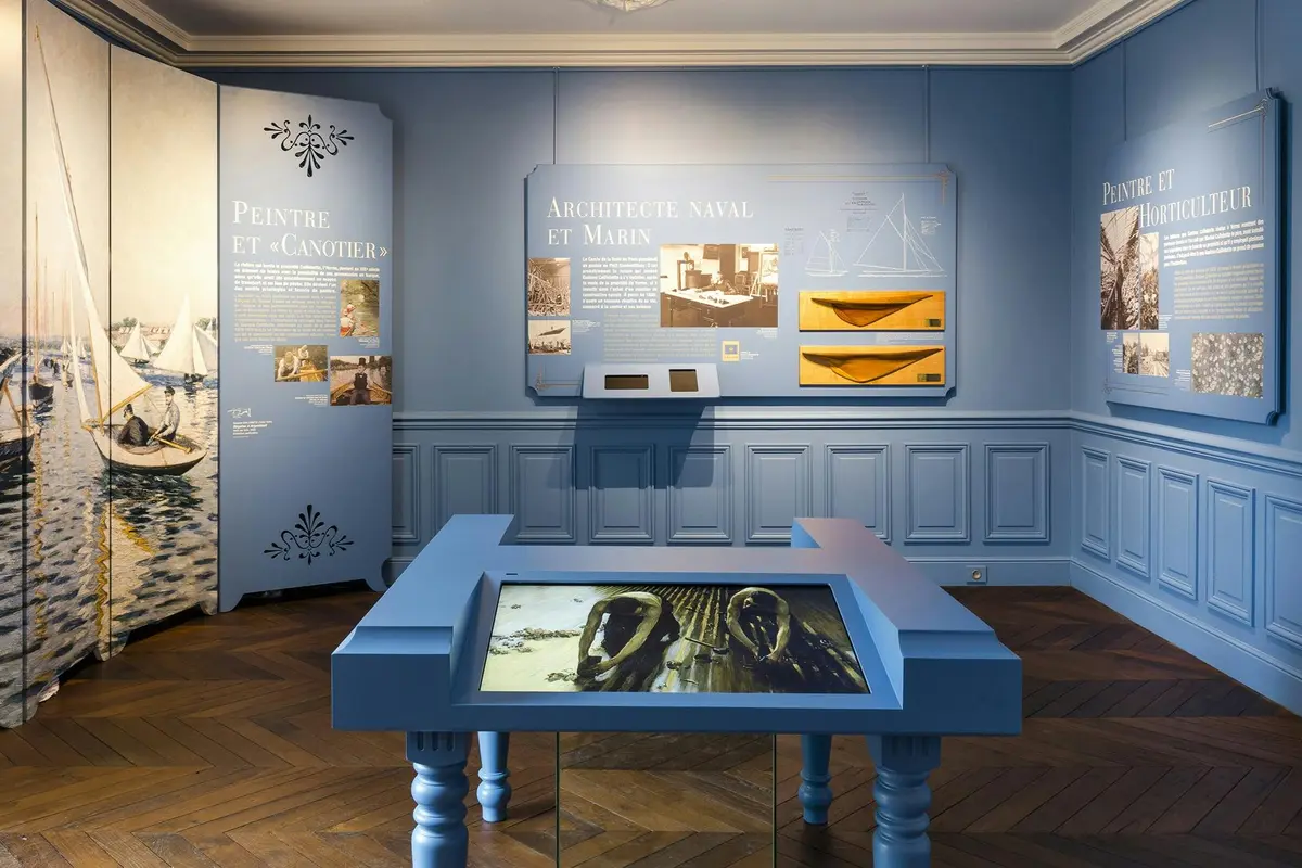 Exposition muséale dans une salle bleue présentant des éléments d'architecture navale, notamment des maquettes et des panneaux descriptifs.