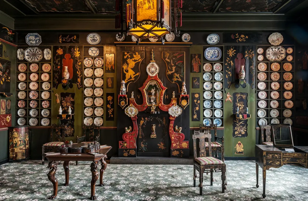 Chambre ornée de plaques murales décoratives, de meubles en bois sombre, de tapis à motifs et d'œuvres d'art murales complexes représentant des dragons et des motifs floraux.