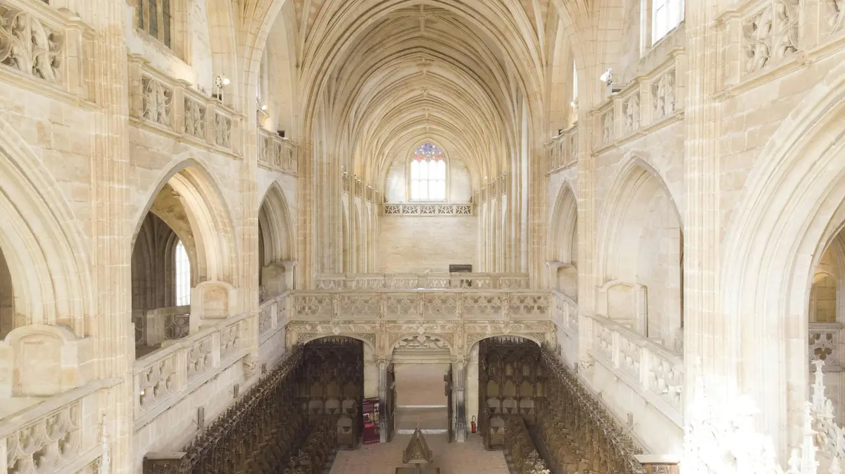 Une cathédrale gothique spacieuse avec de hauts plafonds voûtés, une maçonnerie complexe et des stalles de chœur en bois.