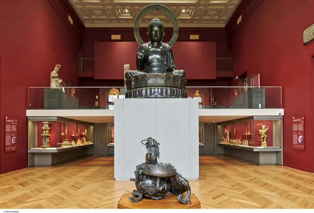 Exposition du musée avec une grande statue de Bouddha sur une plate-forme surélevée et une sculpture de dragon au premier plan.