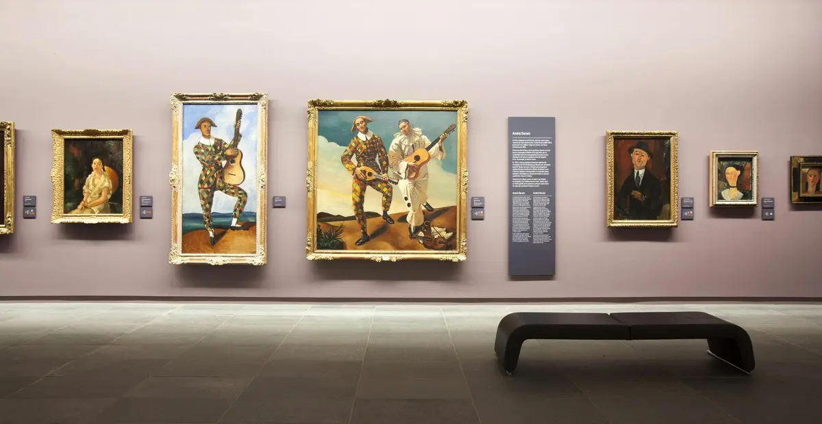 Trois tableaux encadrés sur le mur d'un musée, dont un avec une étiquette et un banc au premier plan.