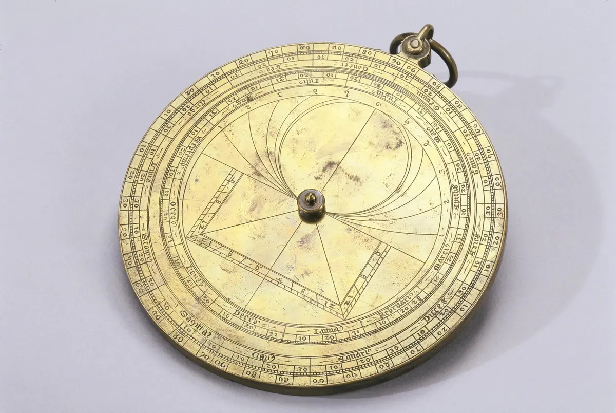 Astrolabe en laiton avec des marques circulaires et des gravures géométriques complexes ; un petit anneau est attaché au sommet.