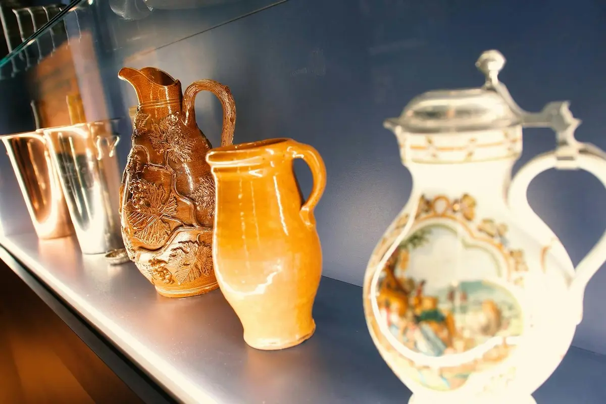 Trois cruches en céramique sont présentées sur une étagère, l'une sculptée de façon complexe, l'autre orange et la dernière peinte avec des motifs détaillés.