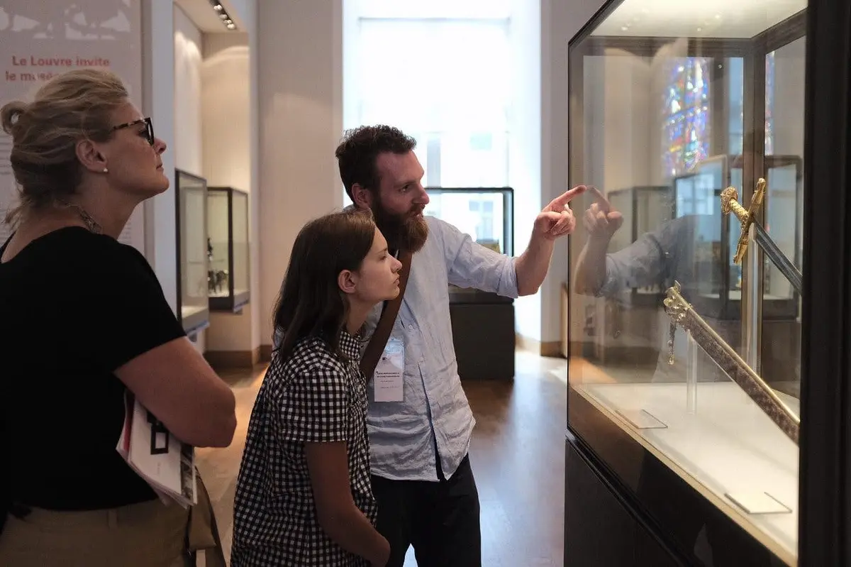 Trois personnes observent les objets exposés dans un musée, l'une montrant du doigt et expliquant tandis que les autres écoutent attentivement.