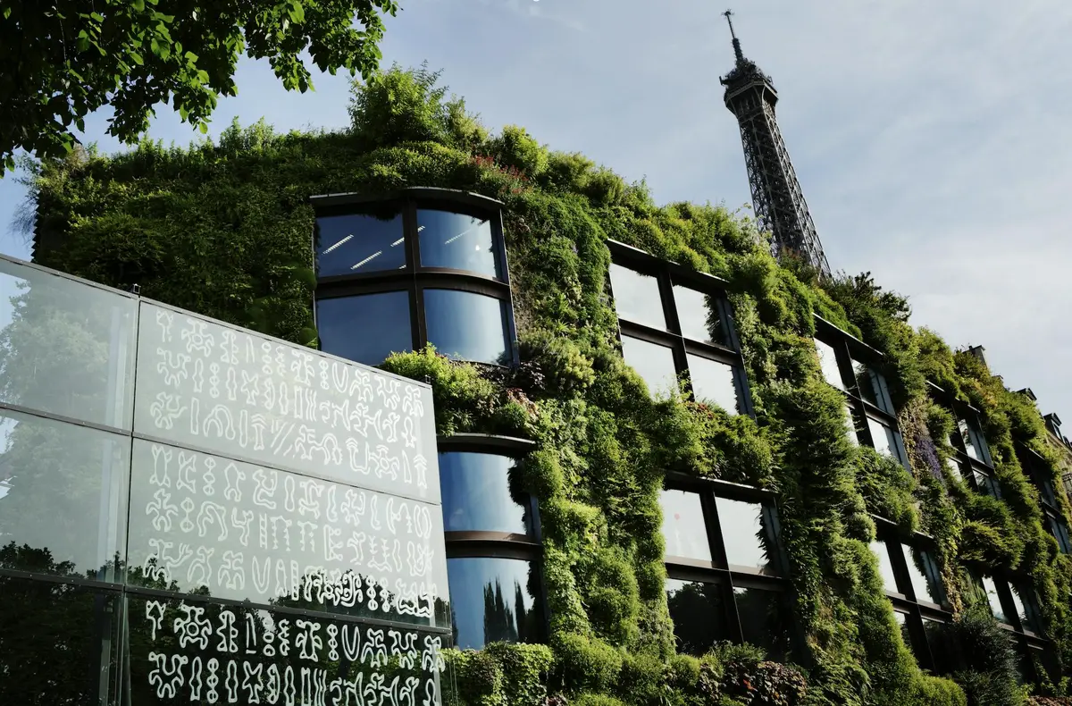Un bâtiment avec un mur végétal, de grandes fenêtres et un panneau adjacent avec des symboles. La Tour Eiffel est visible à l'arrière-plan.