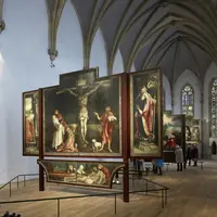 Intérieur d'une cathédrale montrant des retables ornés de peintures religieuses et des visiteurs observant les œuvres d'art. DR