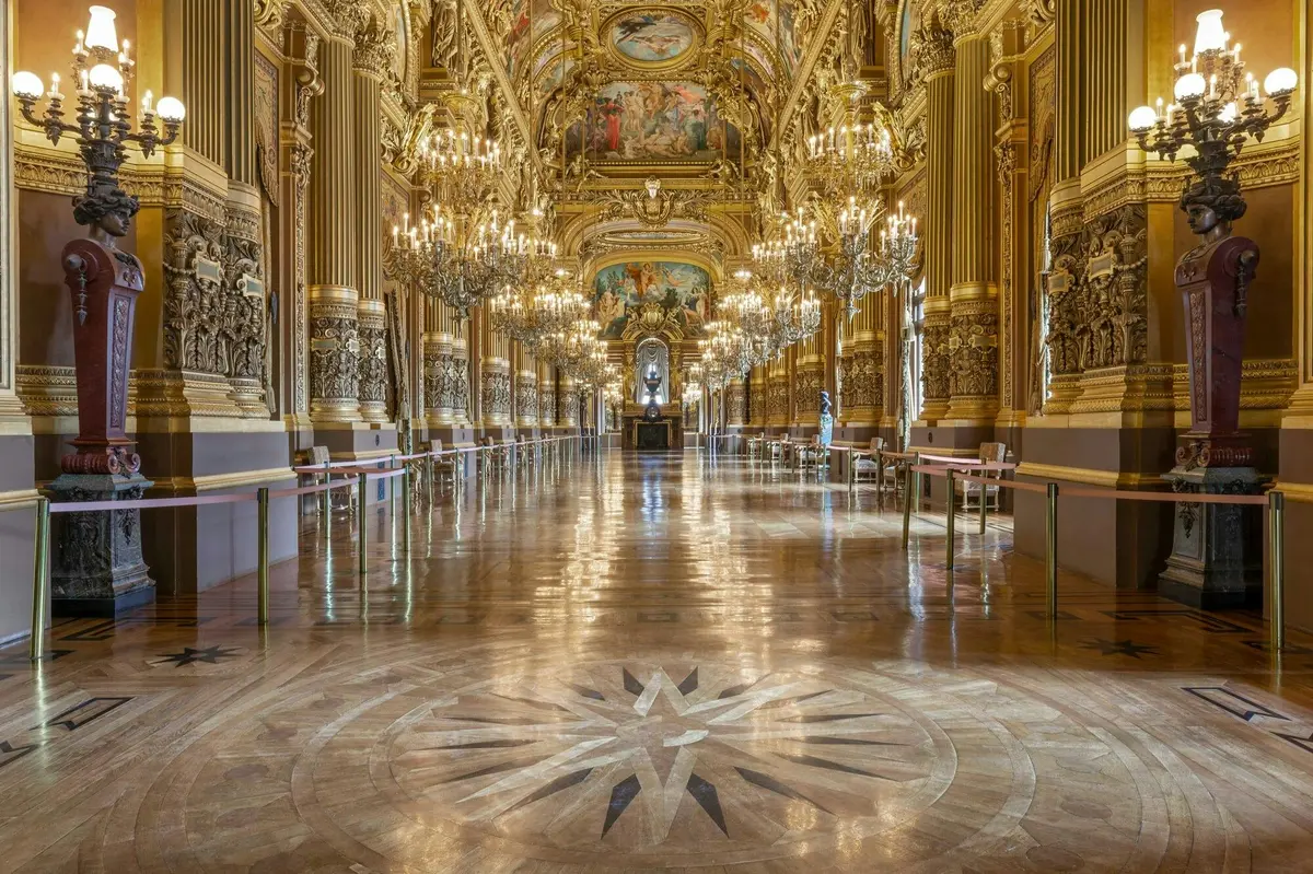 Une grande salle ornée de décorations dorées somptueuses, de lustres et d'un sol ciré, avec un motif central et une statue au loin.