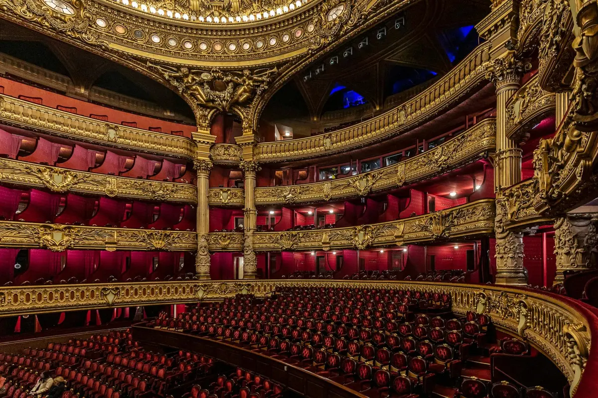 Intérieur somptueux d'un théâtre, avec des décorations dorées raffinées, des sièges rouges et de nombreux balcons.