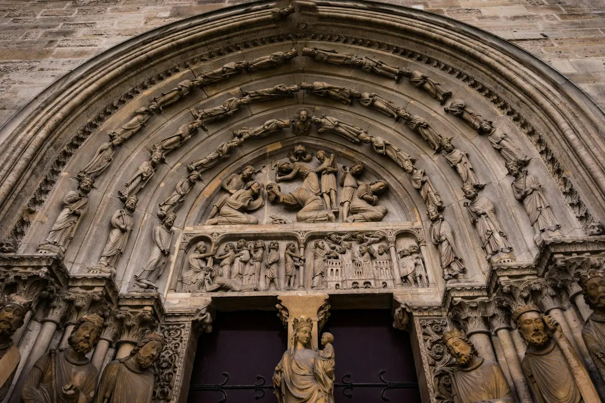 Arcade en pierre sculptée de façon complexe représentant des scènes religieuses au-dessus d'une porte ornée de statues détaillées.