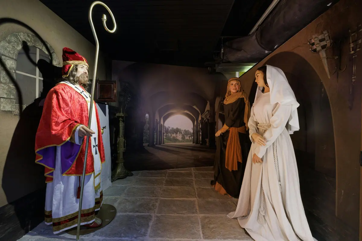 Deux mannequins vêtus de tenues de style médiéval se tiennent dans une pièce faiblement éclairée, avec en arrière-plan une architecture voûtée.