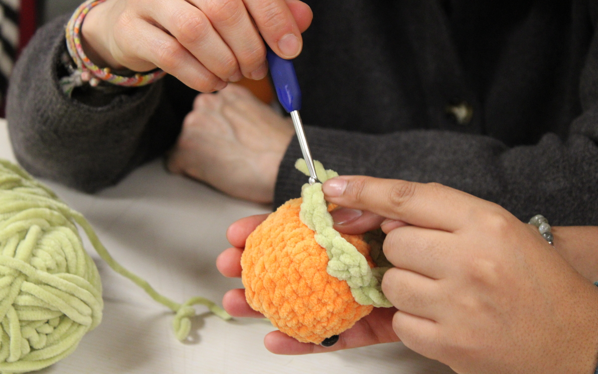Photographie des mains d'une participante de l'atelier créatif peluche en crochet, en train de crocheter une mini orange.