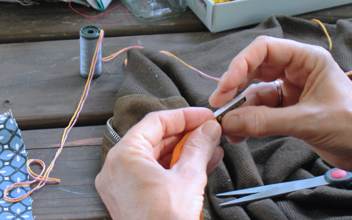 Photographie zoomée de mains tenant du fil de laine orange pour l'atelier réparation couture.