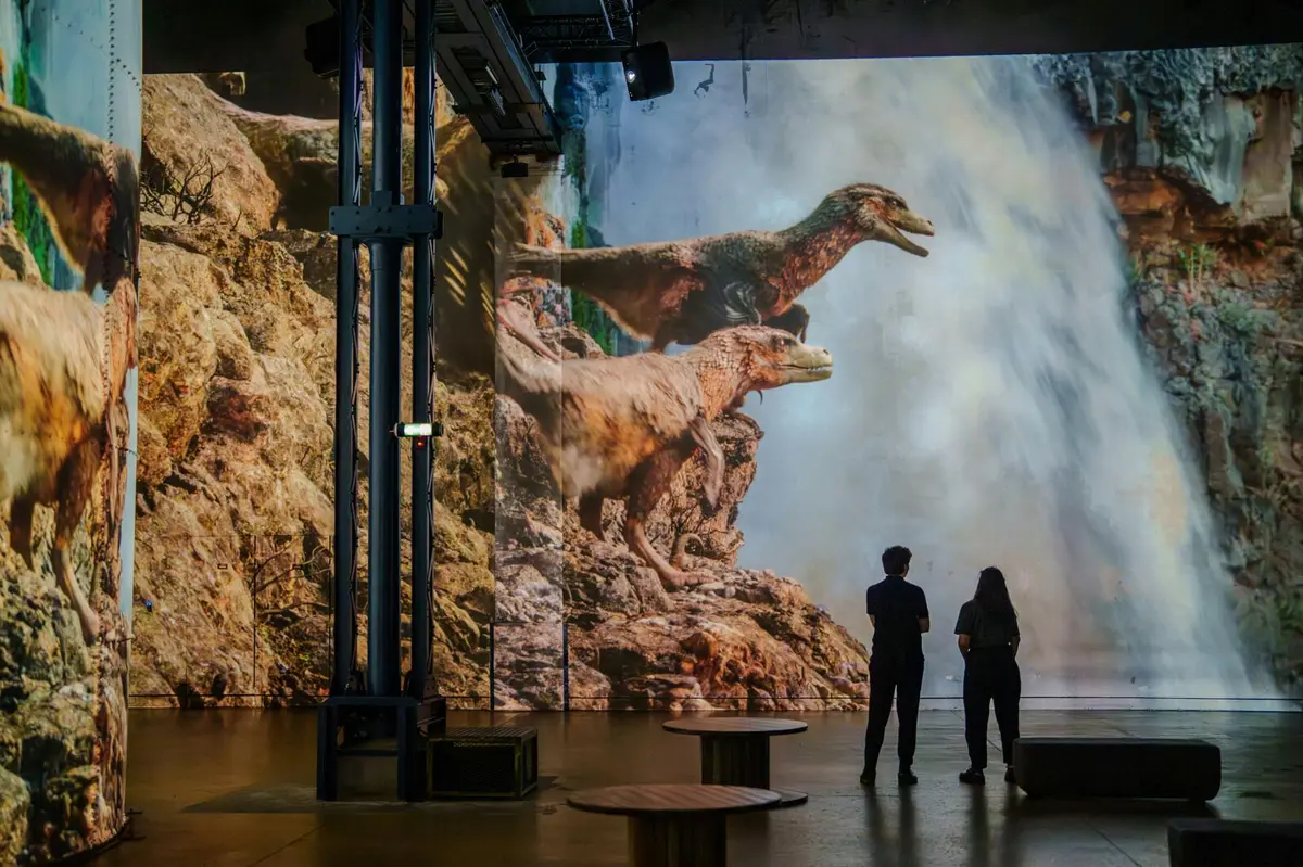 Deux personnes se trouvent dans une salle avec une grande projection de dinosaures sur un fond rocheux avec une chute d'eau.