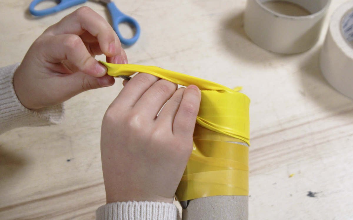 Photographie des mains d’une petite fille en train de fabriquer un instrument de musique avec des matériaux de seconde main.