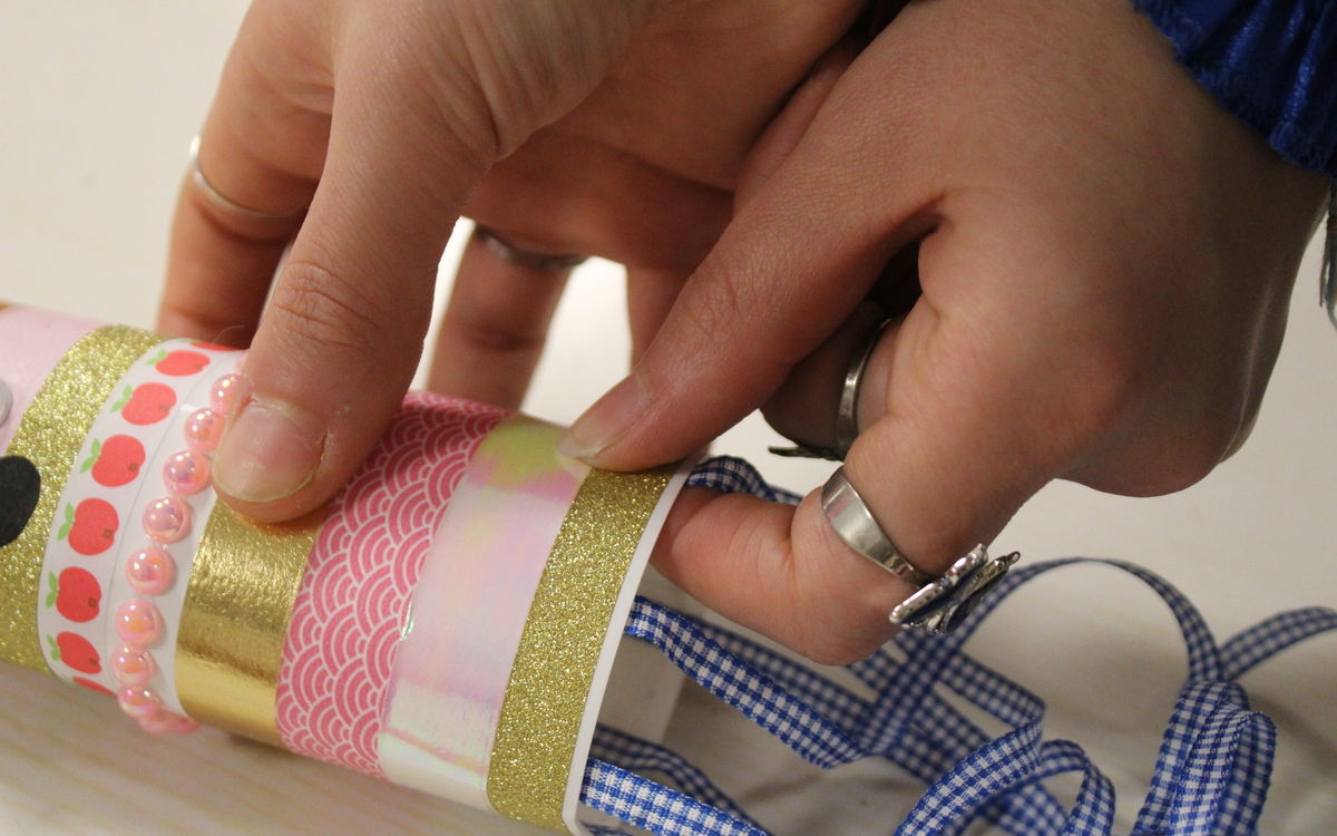 Photo de mains en train de coller des rubans bleus sur une structure en papier afin de créer un poisson.