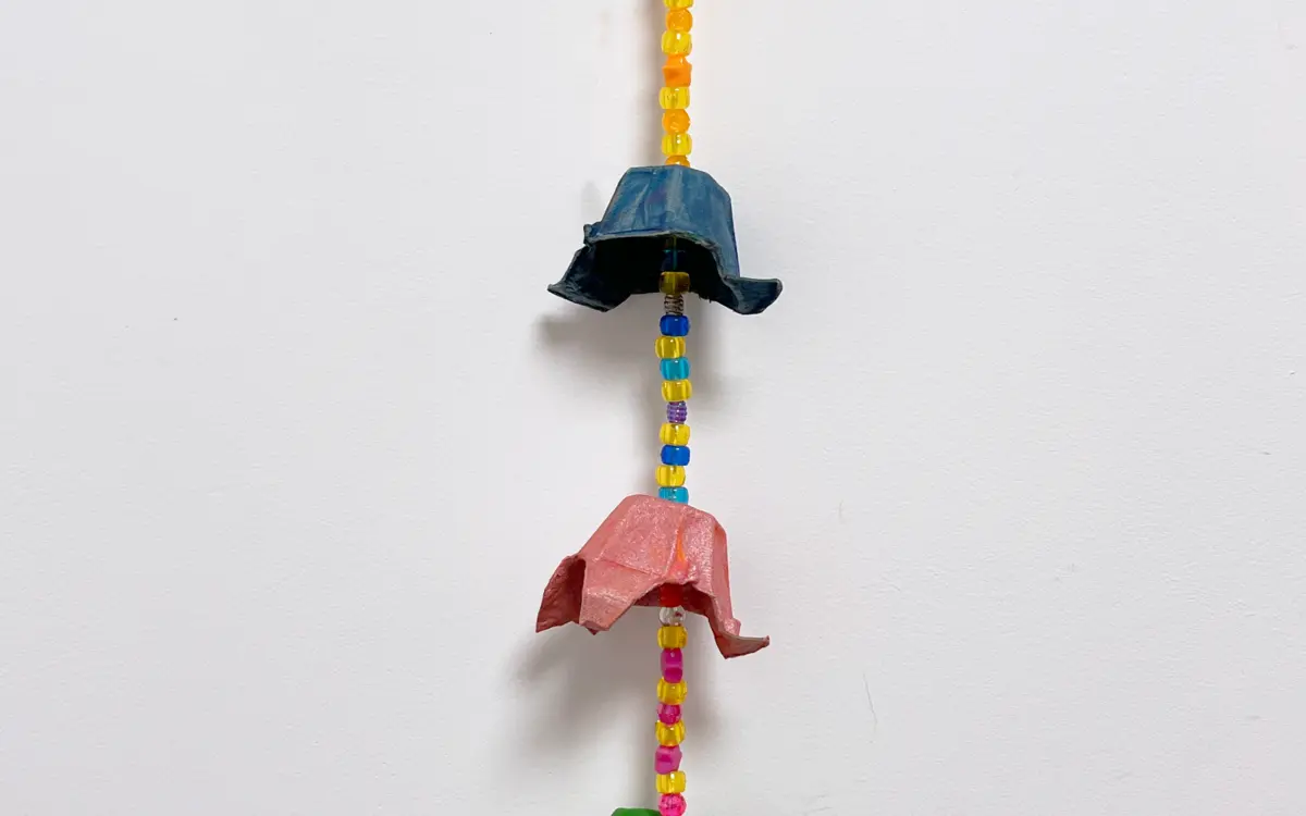 Photographie d'une suspension murale faite à partir de boîtes d'œufs peintes et de perles, le tout de différentes couleurs : rose, jaune, bleu, vert et orange.