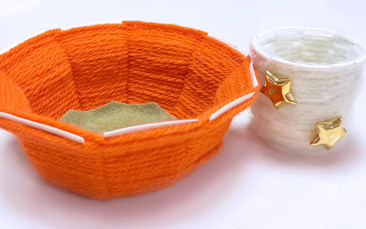 Photographie de deux bols en laines, l'un orange, l'autre blanc avec des étoiles dorées, créés à partir d'assiettes en carton.