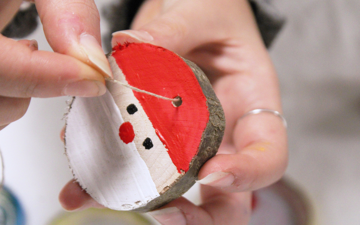 Photographie d'une main tenant un rondin de bois sur lequel a été peint le père Noël.