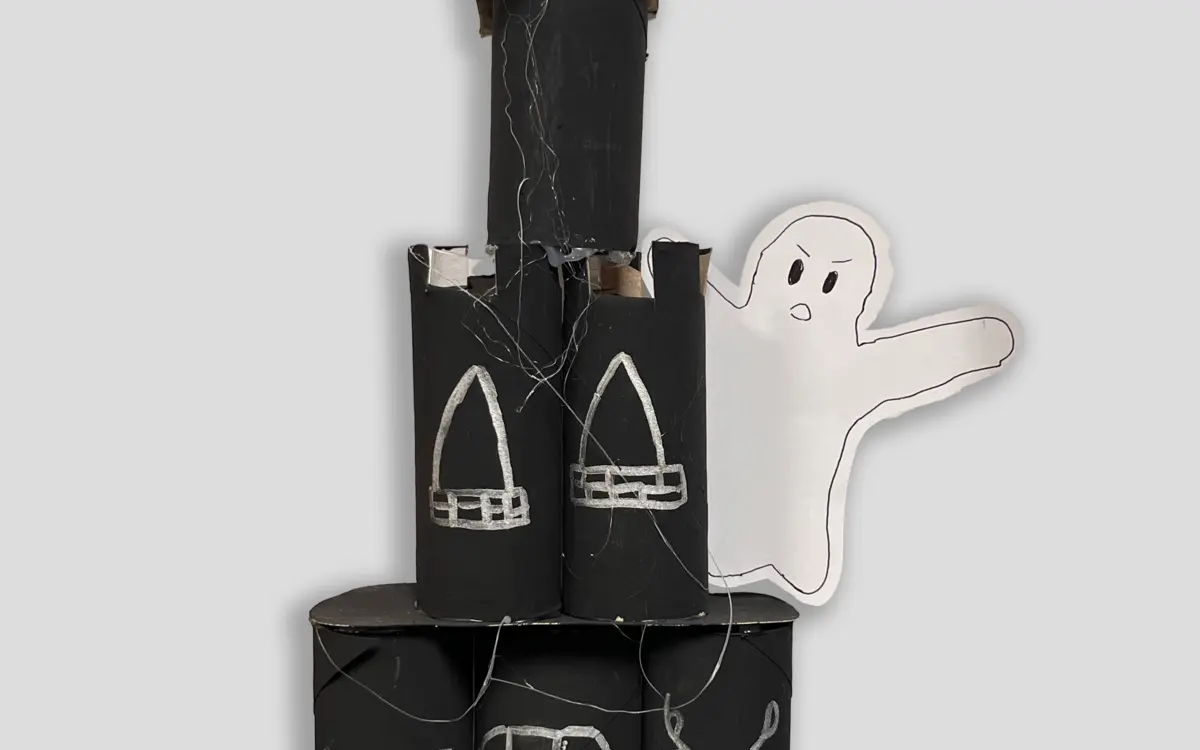 Un château hanté fabriqué et construit à la main. Le château est noir avec des détails blancs et un fantôme fait en papier.