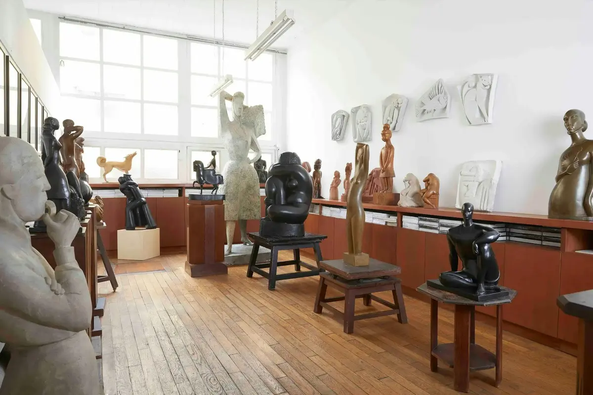 Une salle où sont exposées, sur des socles et des étagères, diverses sculptures aux formes humaines et abstraites, sous un éclairage vif.