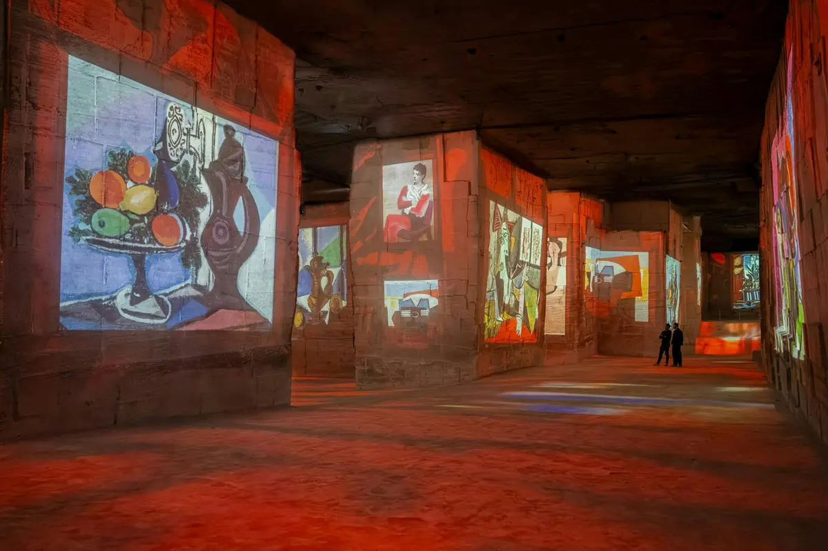 Une exposition d'art immersive avec des peintures colorées projetées sur des murs de pierre, avec quelques visiteurs qui observent les expositions.