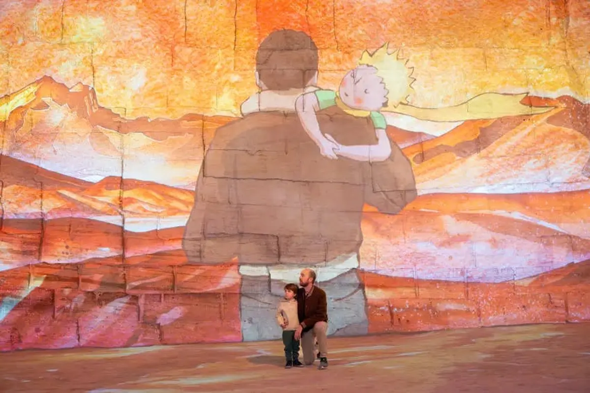 Un homme agenouillé à côté d'un enfant devant une grande projection murale d'une illustration représentant un homme et un petit garçon sur son dos.