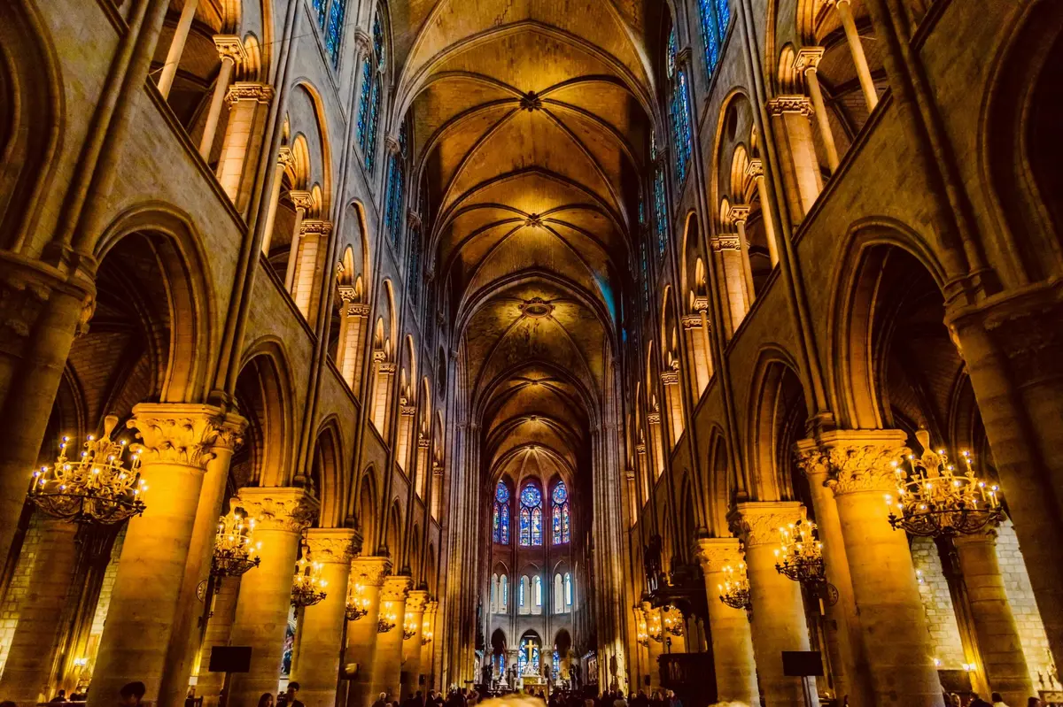 Intérieur d'une grande cathédrale avec de hauts plafonds voûtés, des colonnes ornées, des lustres brillants et des vitraux en arrière-plan.