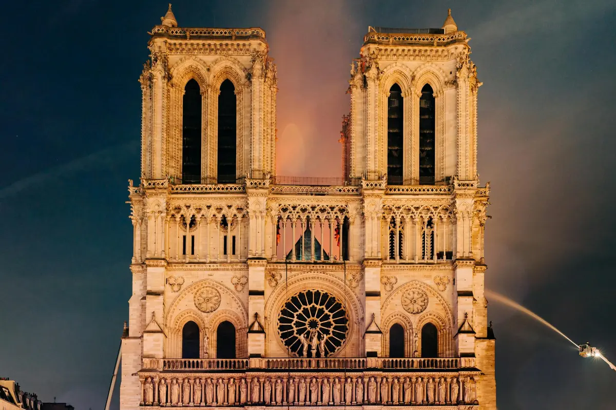 Vue de face de la cathédrale Notre-Dame avec ses tours jumelles emblématiques et sa rosace centrale illuminée dans un ciel sombre.