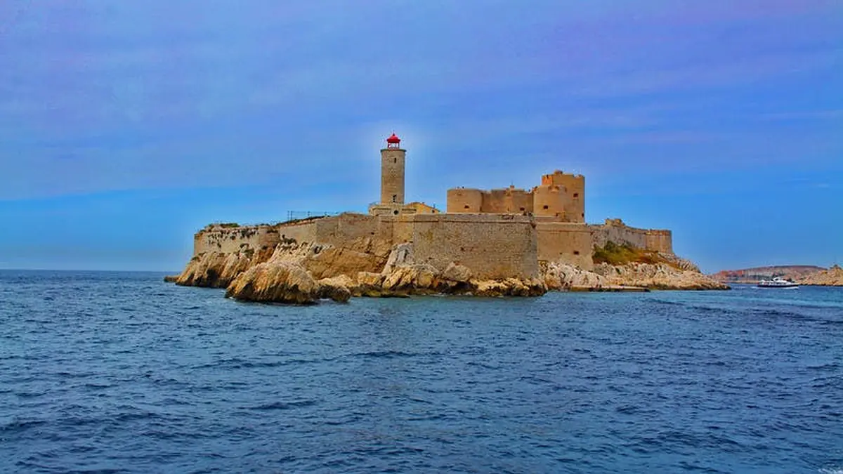 Forteresse en pierre avec un phare sur une île rocheuse, entourée d'un océan bleu sous un ciel clair.