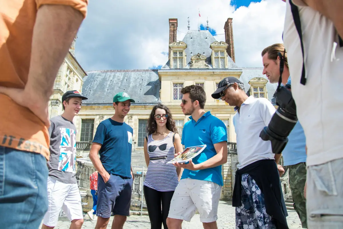 Un groupe de personnes se tenant à l'extérieur près d'un bâtiment historique, avec un ciel nuageux en arrière-plan.