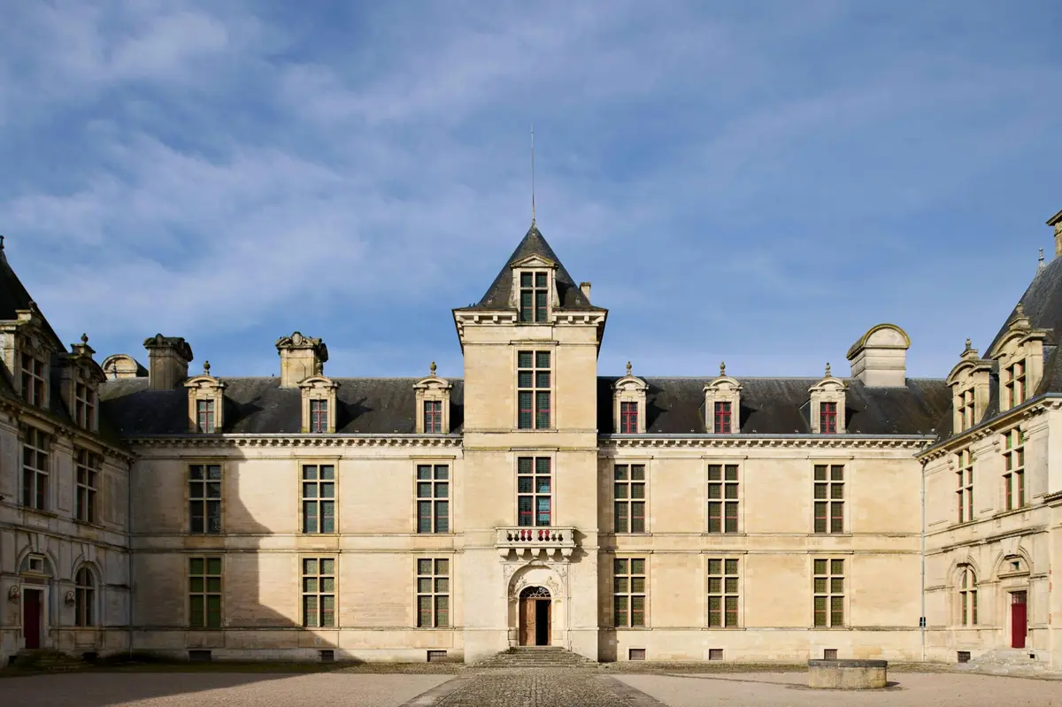 Un ch&acirc;teau historique sym&eacute;trique avec une tour centrale, des lucarnes et une entr&eacute;e vo&ucirc;t&eacute;e, sur fond de ciel bleu.